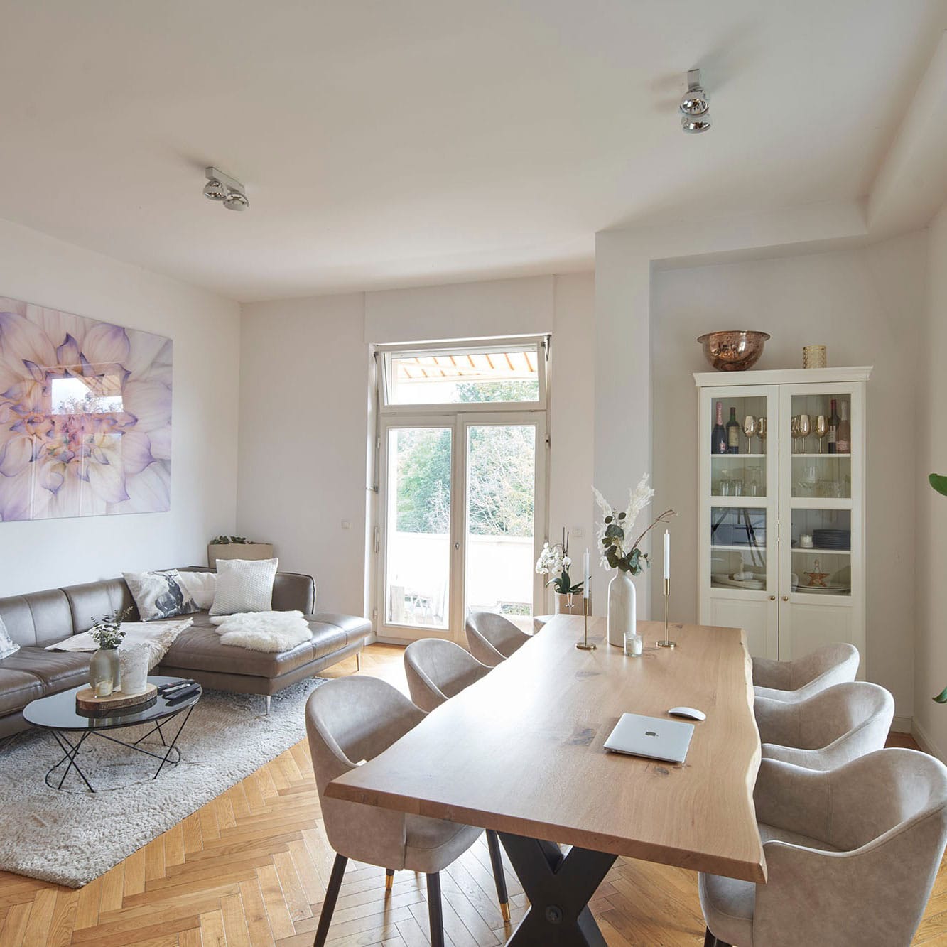 Heller, moderner Wohn- und Essbereich mit einem Holztisch, hellgrauen Stühlen, einem Ecksofa und Glastüren, die auf den Balkon führen. Genießen Sie exklusives Seniorenwohnen in Sasbach – modernes Wohnen im Alter in der Villa Erlenbad.